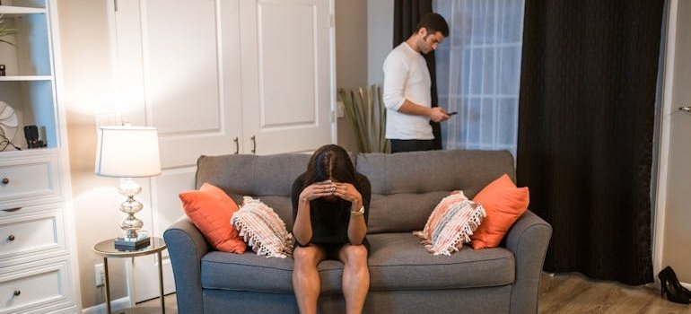 Woman sitting on a couch while her partner is looking at his phone.