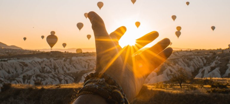 A person's hand against the sunset with hot air balloons in the background representing healthy coping skills while looking at hot air balloons and sunset.