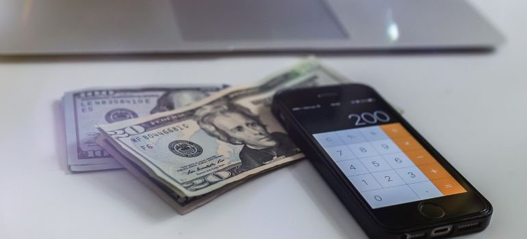 Some dollar bills next to a mobile phone.