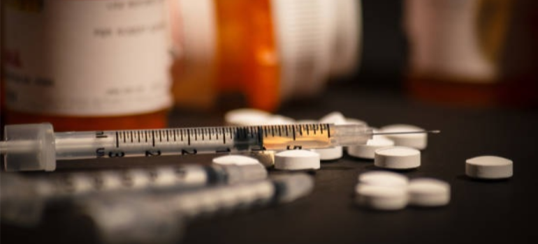 A syringe next to pill bottles.