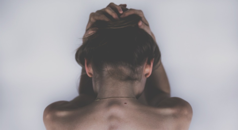 The bare back of a depressed woman in need of heroin addiction treatment.