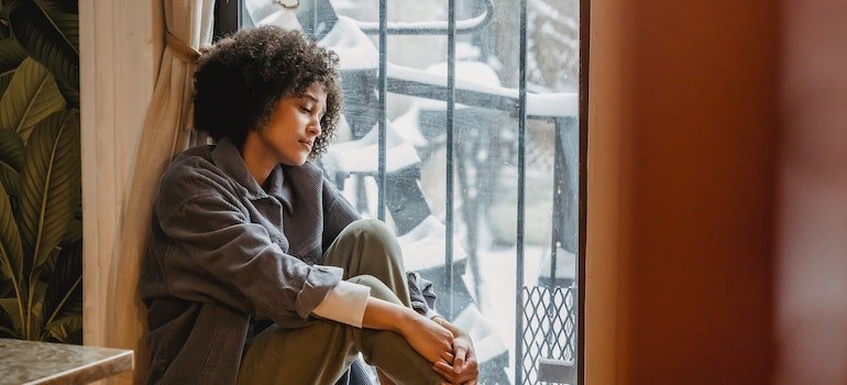 a person sitting on the floor and looking out the window thinking Does CBD play a role in addiction recovery?