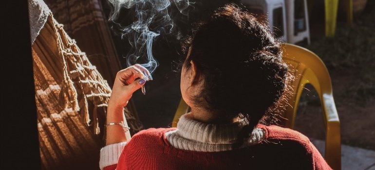 Person wearing a red sweater smoking next to a yellow plastic chair