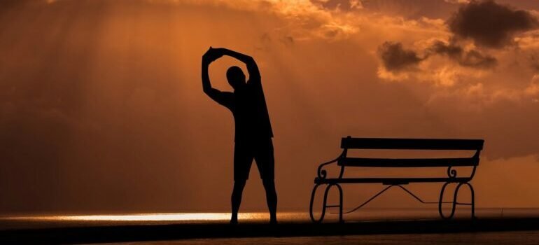 a silhouette of a man stretching near a bench