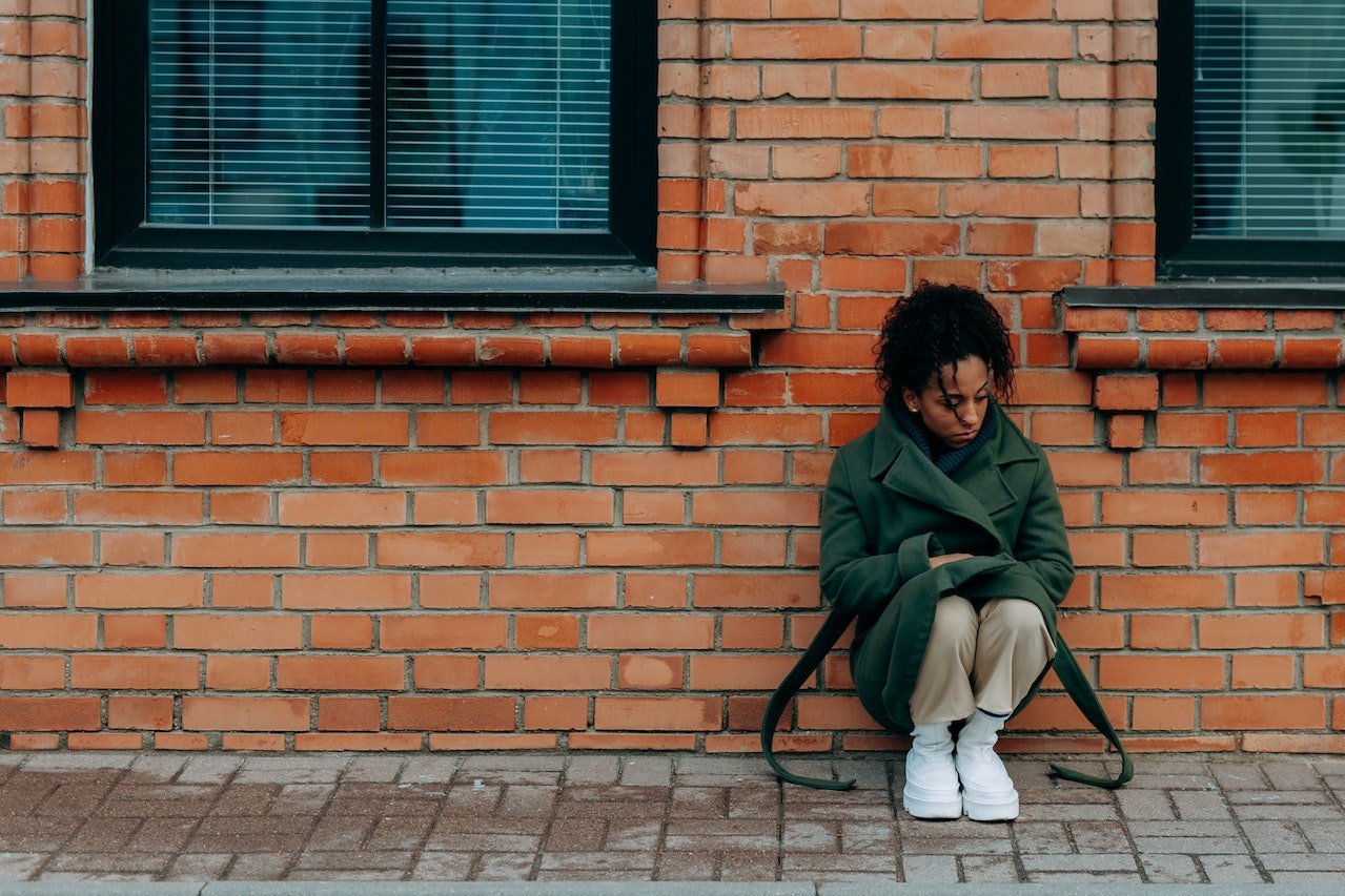 Depressed woman squatting next to a brick wall and experiencing effects of crack cocaine