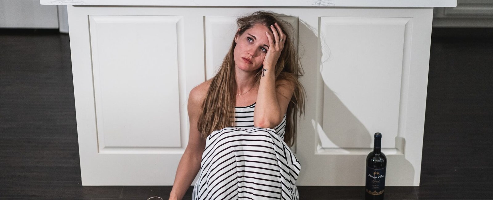 Woman sitting on the floor next to an empty bottle to symbolize alcoholism and depression