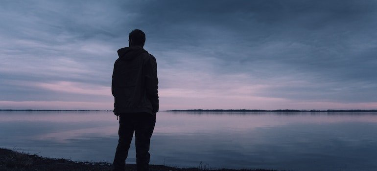 Man sitting alone by a body of water in one of the destinations to visit after rehab in PA