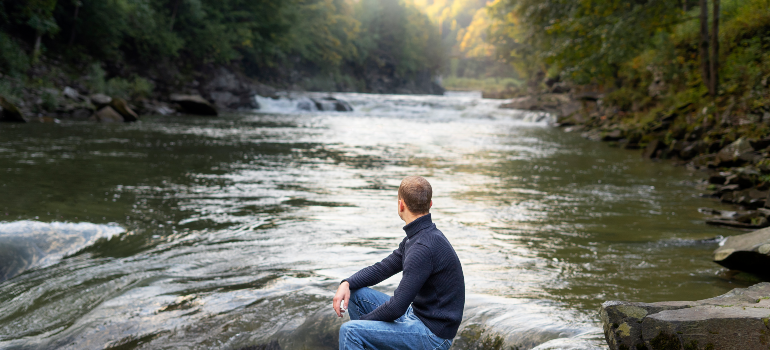 a man sitting on a rock embracing the beauty of Pennsylvania's nature,, representing how to Start Your Day Sober in Pennsylvania
