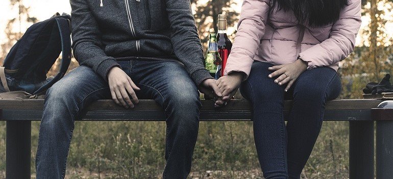Couple sitting on bench with bottle.