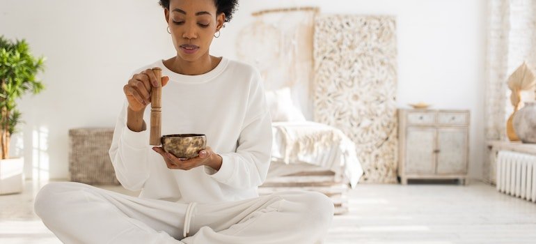 a woman in white sitting on a floor and holding a golden bowl