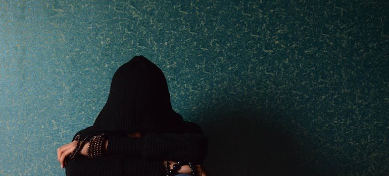 woman with a black hood over her face sitting in front of a wall