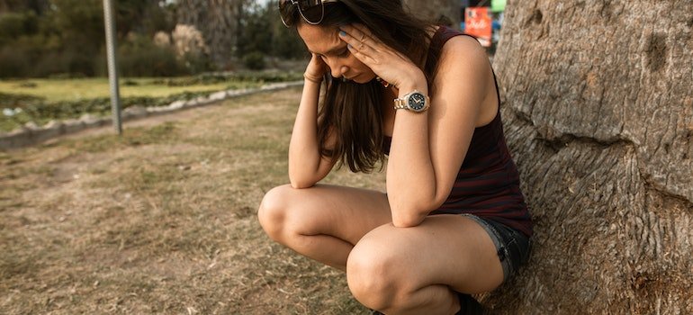woman squatting by a tree with her face in her hands