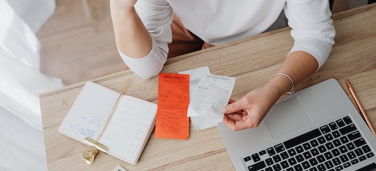a woman at the desk holding a white piece of paper and reading about how to financially recover after addiction