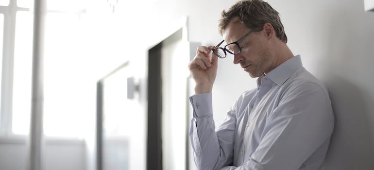man leaning against a wall taking off glasses