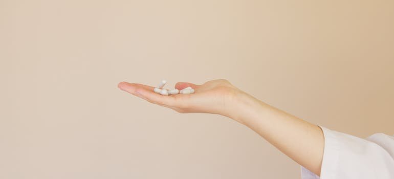 Crop female pharmacist with pile of white pills on palm comparing Gabapentin vs Xanax 