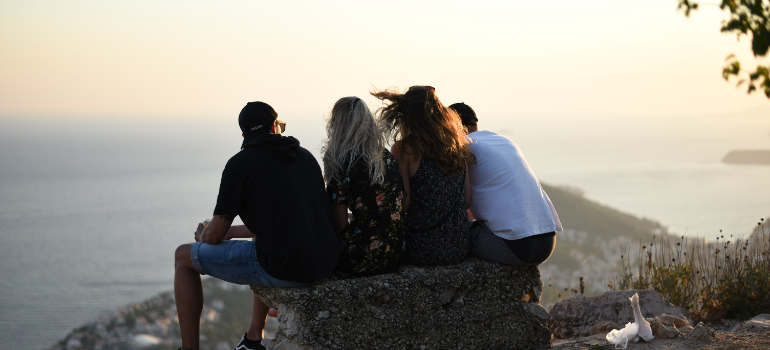 friends sitting on a rock at the top of a hill and talking 