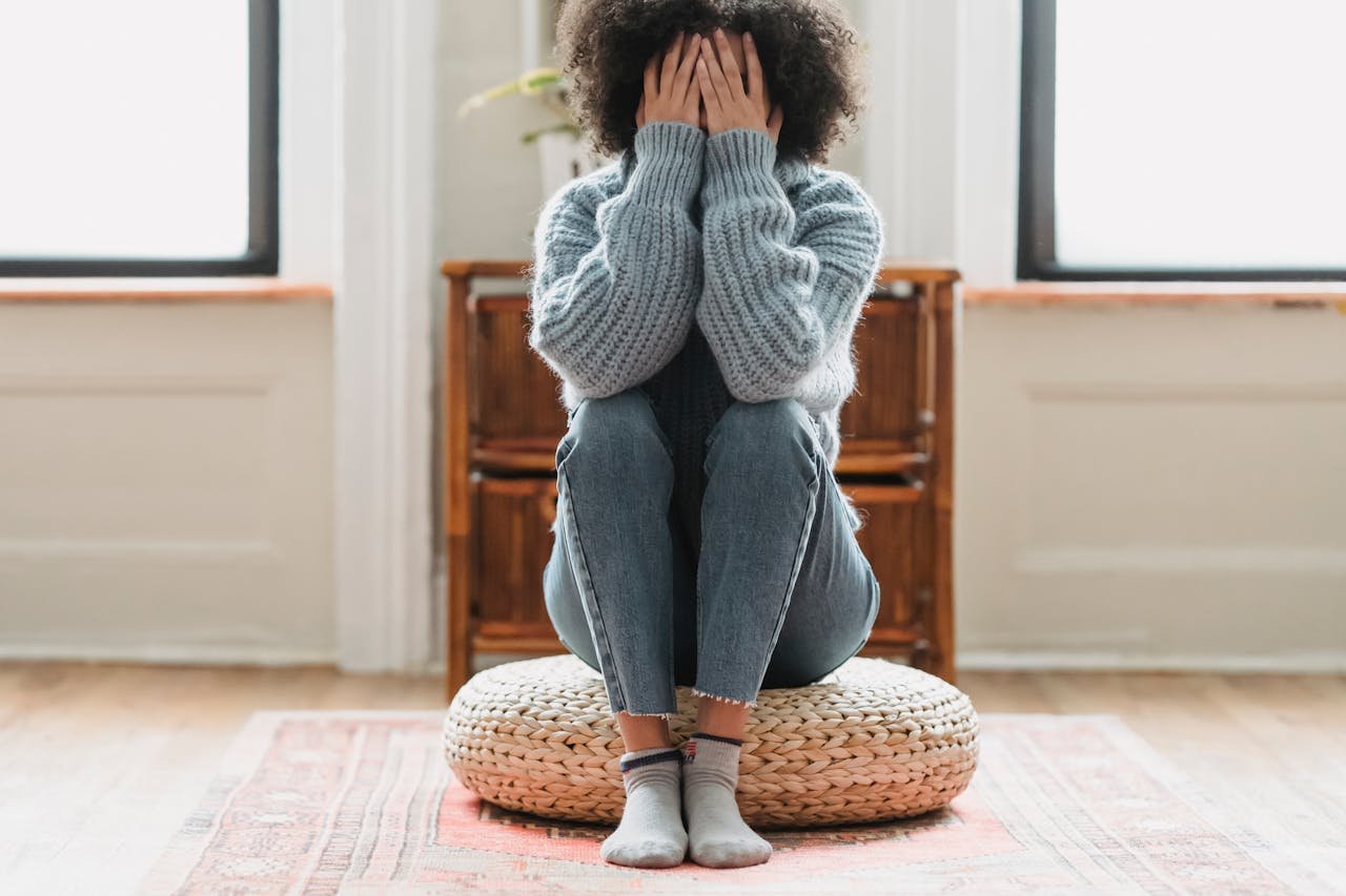 A teenage girl sitting on the floor with her hands on her face