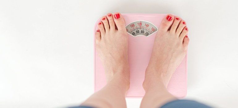A woman on a scale after losing weight caused by liver damage from alcohol.