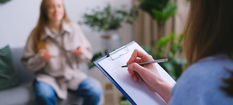 woman taking notes on her clipboard and talking to her client about the benefits of psychiatric care in addiction treatment