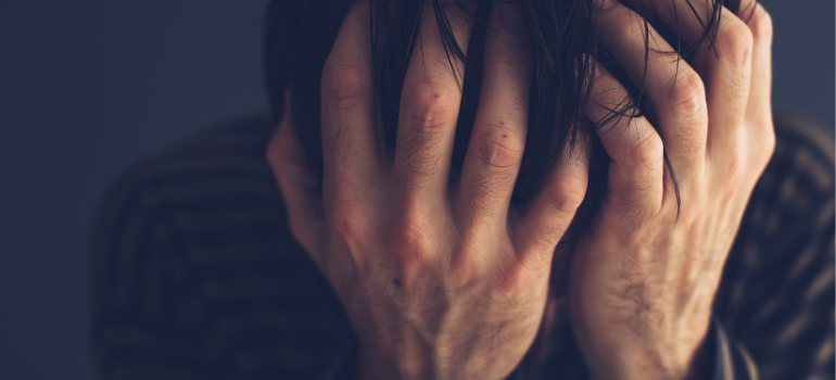 A person covering their face with their hands in distress wondering how long does heroin stay in your system