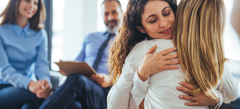 Two young women hug in the context of group therapy