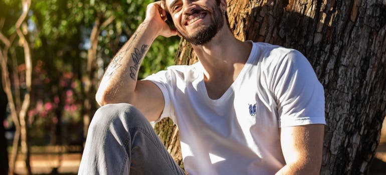 a happy man leaning against a tree