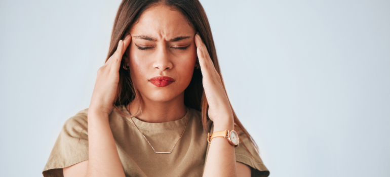 A woman with her eyes tightly closed showing discomfort and holding the sides of her forehead with her hands. going through the Xanax withdrawal symptoms