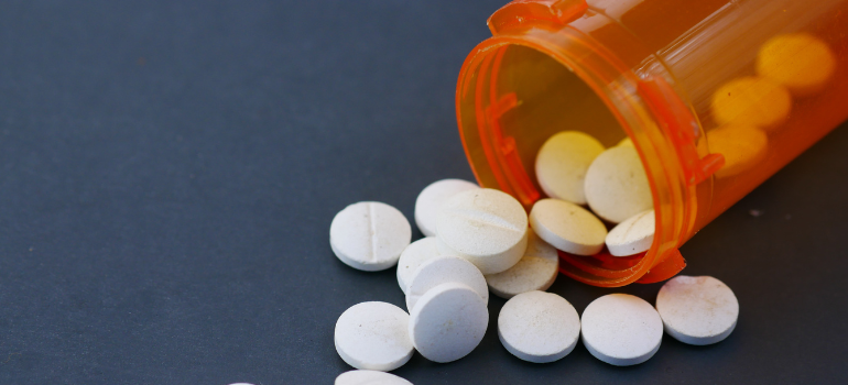 A small orange plastic bottle out of which several white pills come out