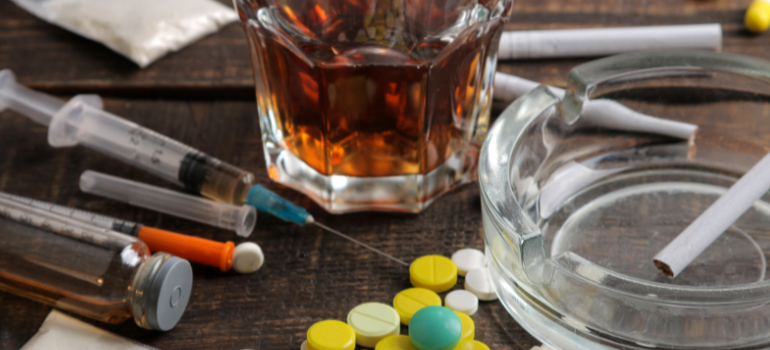 Shots, a whiskey glass, some cigarettes and one barely smoked on an ashtray, and pills on the table