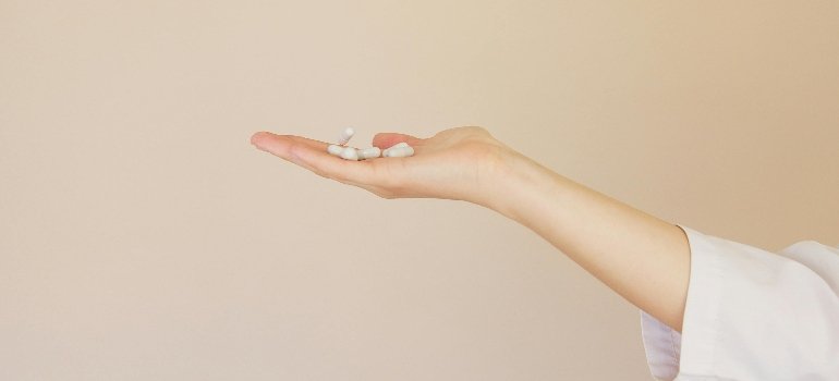 Crop female pharmacist with pile of white pills on palm