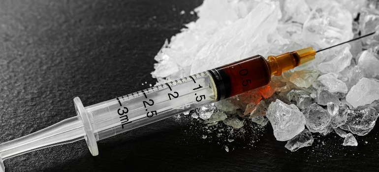 A syringe lies on top of clear bath salts