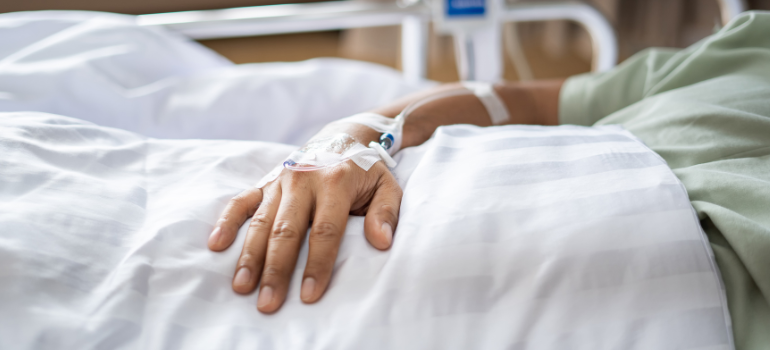 The hand of a hospitalized person in bed receiving an IV