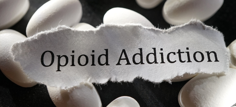 white pills on a black background, a piece of paper in the center that has opioid addiction printed on it.