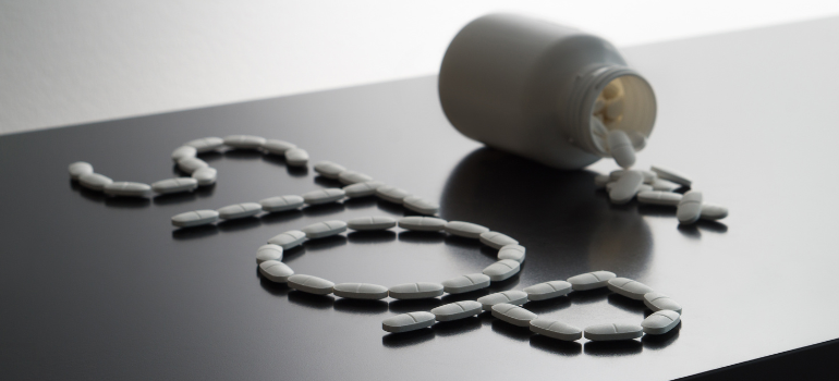 A white bottle of pills out of which white pills come out spelling out STOP.