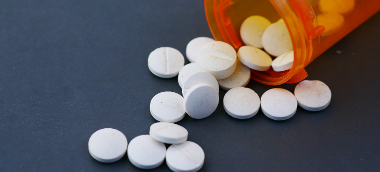 An orange bottle of pills out of which several round white pills come out.