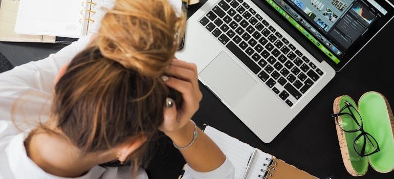 Woman holding her head in destress while looking at her laptop.