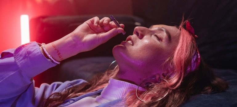 A woman is lying on the bed smoking Salvia.