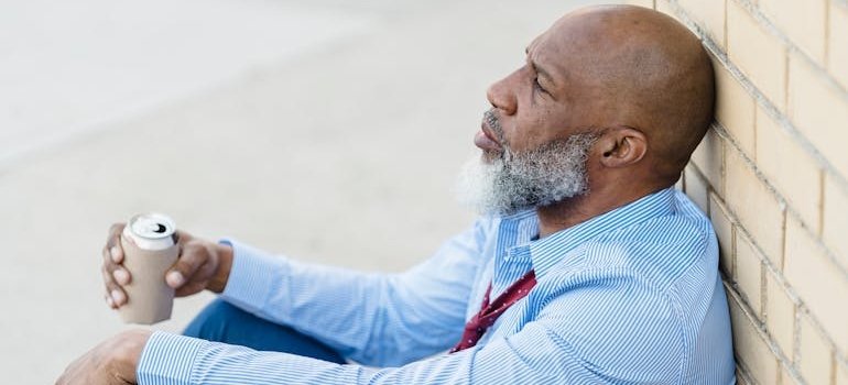 Man leaning against a wall and drinking beer wondering can you drink rubbing alcohol