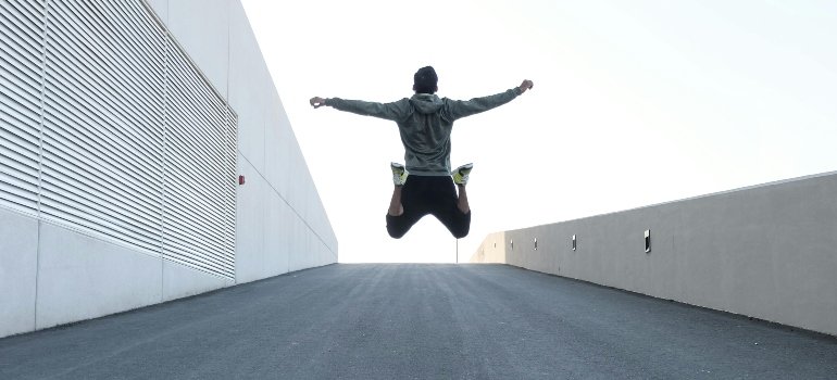 A man in a grey hoodie is jumping with open arms.