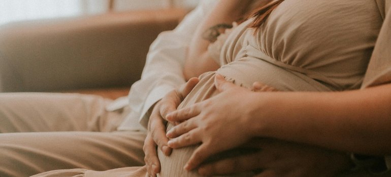 A man and a pregnant woman are sitting on the couch holding a woman's belly.