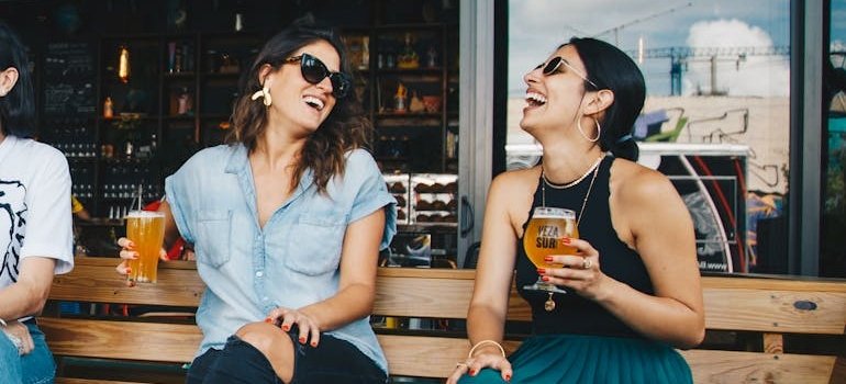 Two women drinking beer and laughing while experiencing personality change when drinking alcohol.