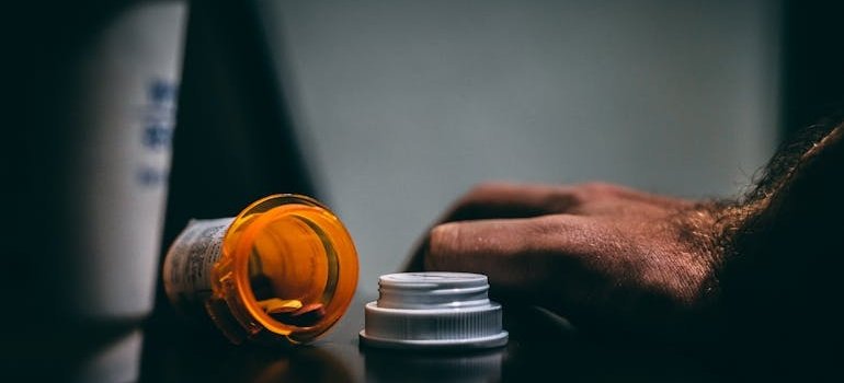 Person's hand next to a spilled pill bottle.