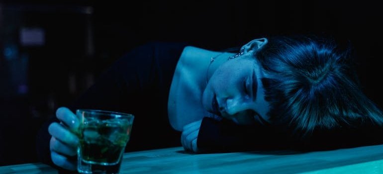 Woman sleeping at the bar and holding a glass of whiskey.