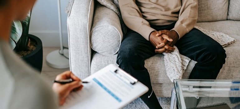 Woman writing in a clipboard and talking to her patient about alcoholic relapse after long term sobriety.