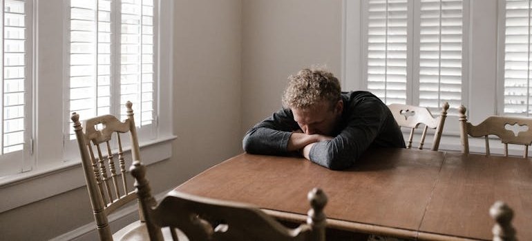 Man sitting at a table and thinking about how to help adult child with addiction.