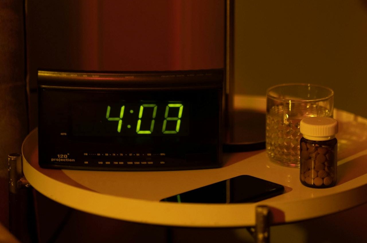 Alarm clock, pills and a phone on a nightstand,