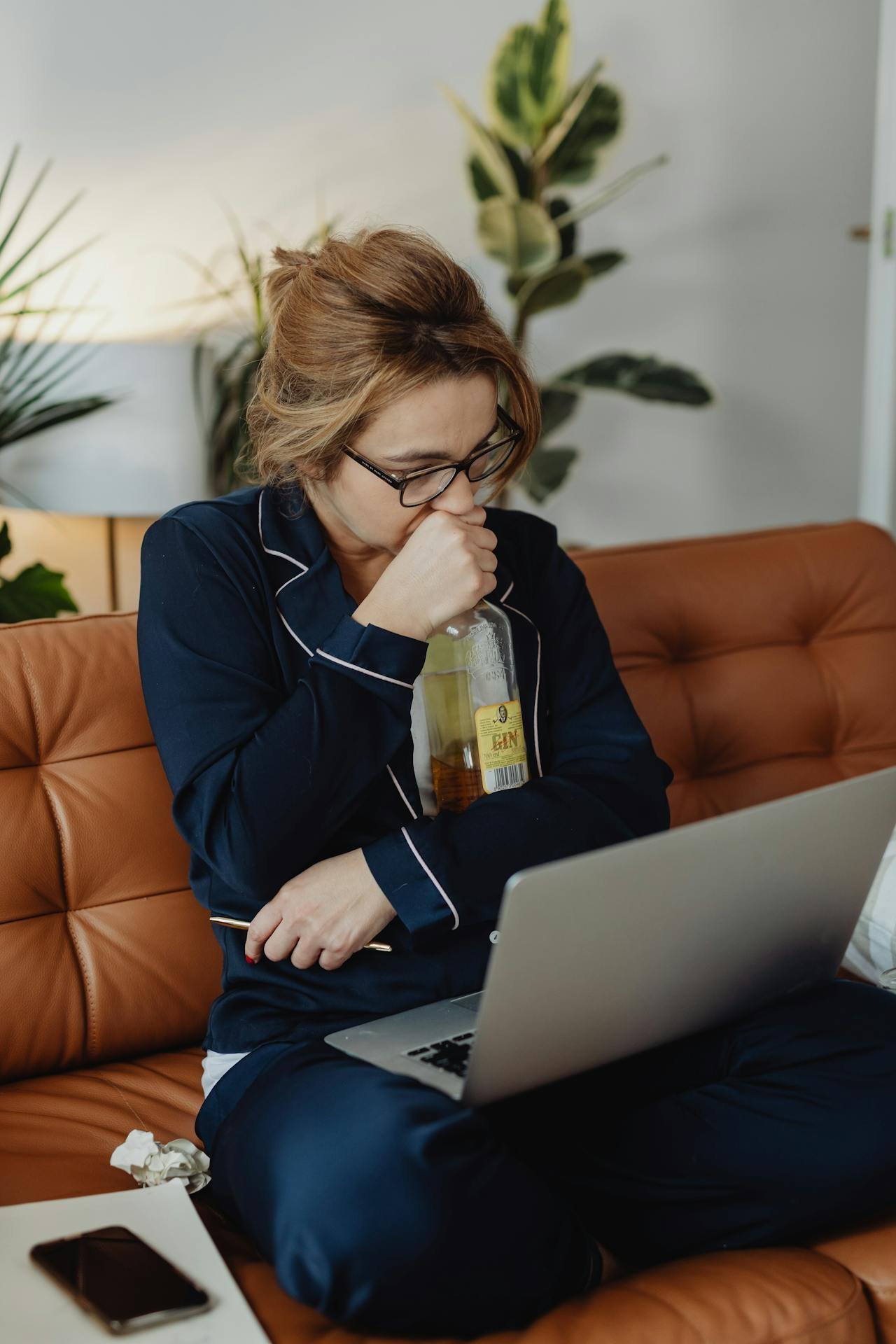 Woman hugging an alcohol bottle while looking at her laptop.
