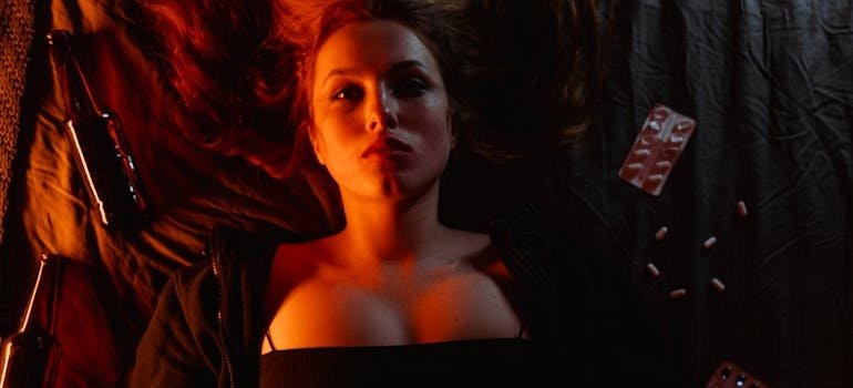 Woman lying on the bed next to beer bottles and pills.