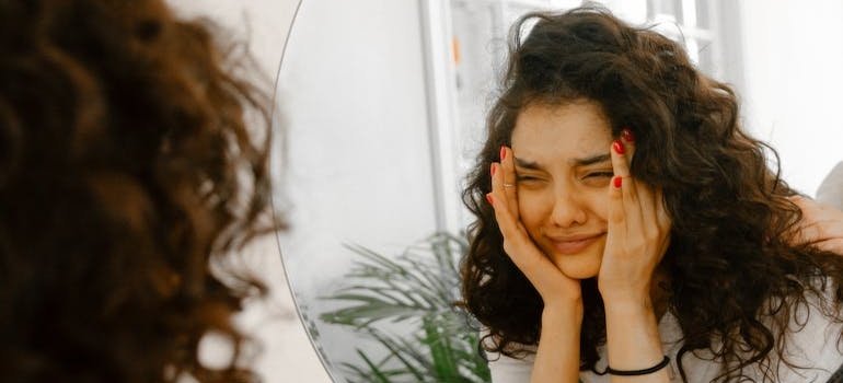 Woman looking at herself in the mirror and holding her head.