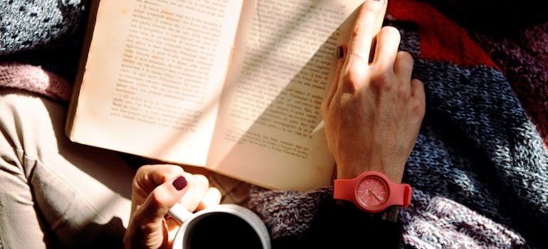 Person sitting in a bed and drinking coffee and reading a book.